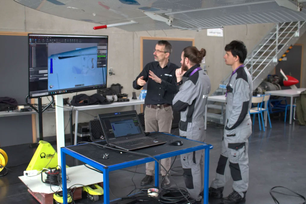 Three people looking at a screen displaying a 3D image