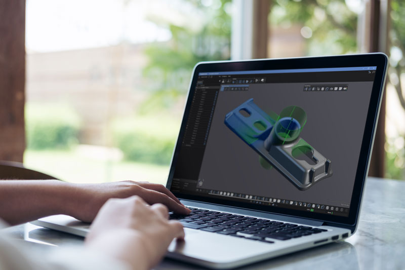 Person in front of a laptop displaying a scan and CAD model of a casting part in Creaform Metrology Suite’s Scan-to-CAD module