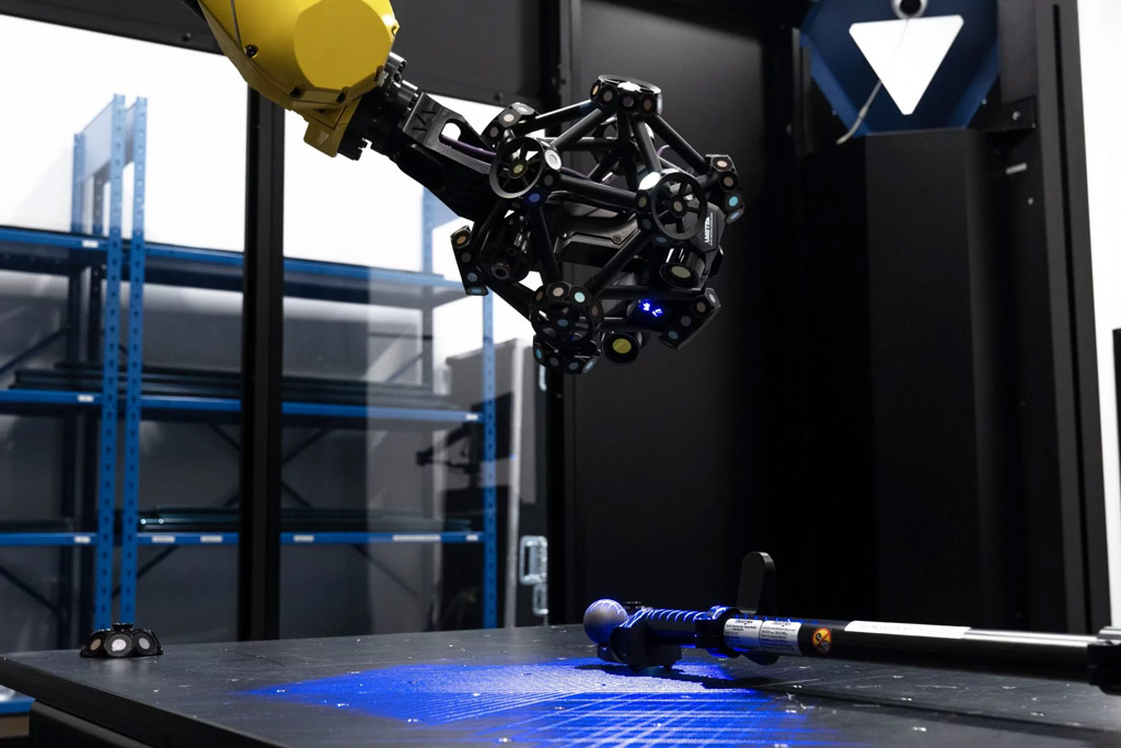 A MetraSCAN 3D-R robot-mounted optical CMM scanner measuring a calibration tool in a metrology cell