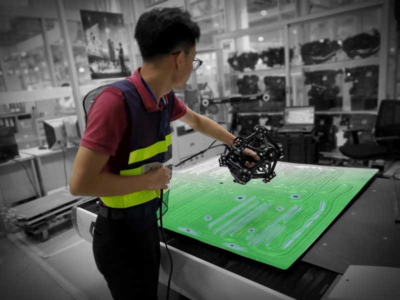 Employee wearing a safety vest using a MetraSCAN 3D scanner to measure a flat sheet metal part with colormap overlay
