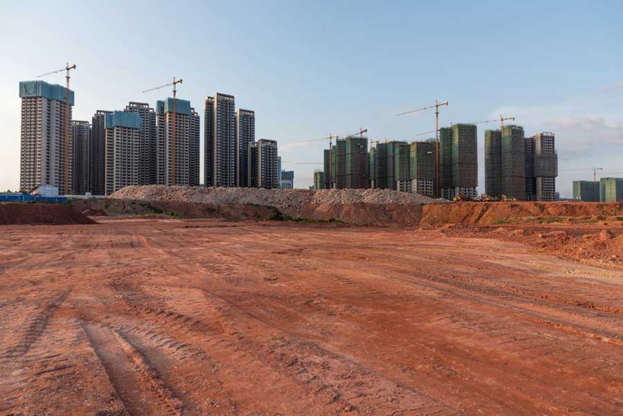 Several high-rise buildings surrounded by tall yellow cranes with a large construction site in the foreground