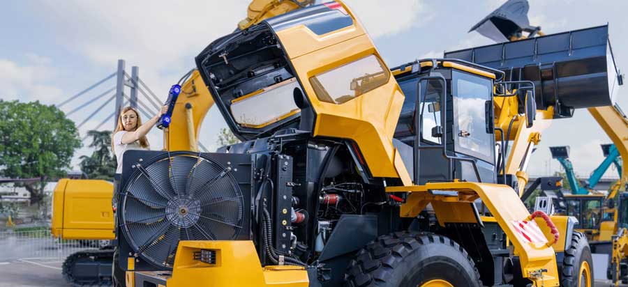 Mujer que utiliza el escáner de la serie HandySCAN MAX para escanear el interior del capó de un cargador frontal amarillo y negro