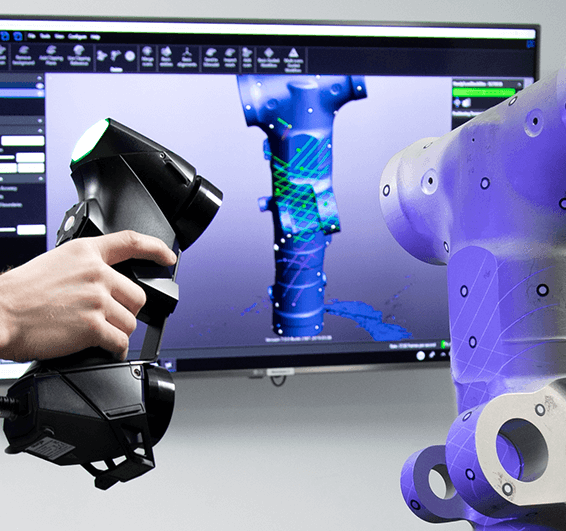Close-up of a Creaform HandySCAN 3D scanner being used to scan a mechanical component, with the resulting 3D model and analysis displayed on a monitor in the background.