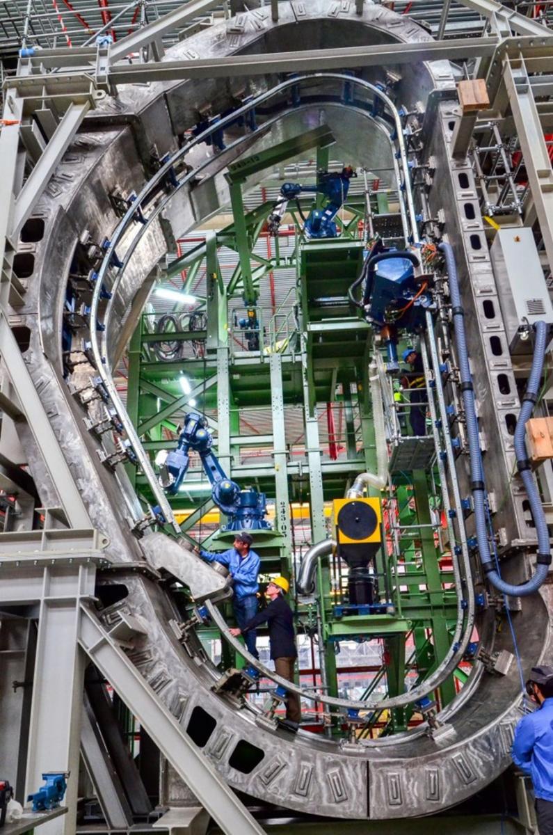 Wide view of two engineers inside a complex part of a nuclear tokamak part. 