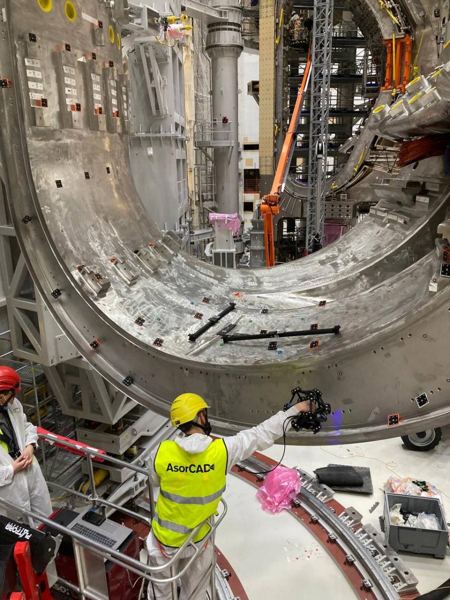 Wide view of two engineers inside a complex part of a nuclear tokamak part. 